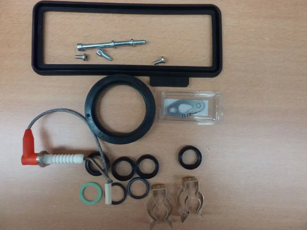 Zubehörset von Remeha, bestehend aus Dichtungen, Befestigungselementen, einem Filter und einem Kabel, auf einer Holzoberfläche angeordnet.